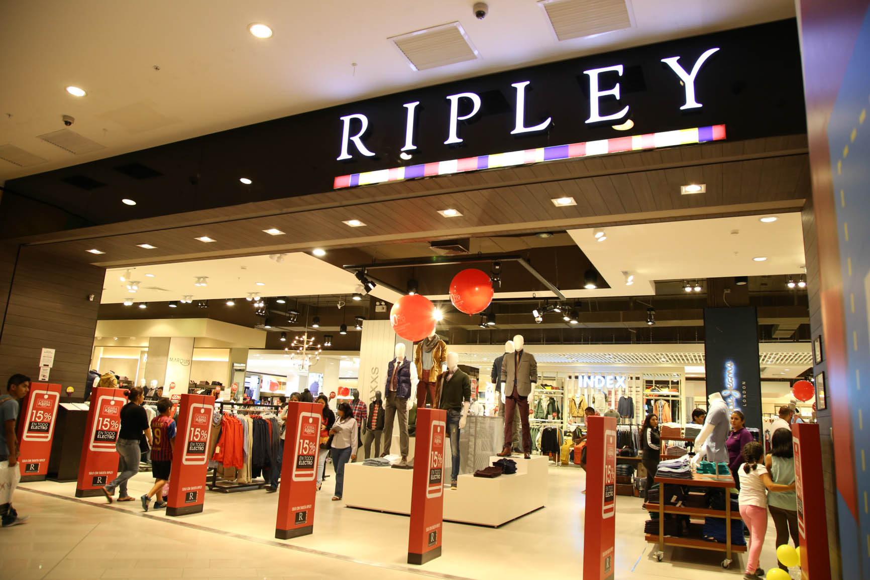 Vista del ingreso a una tienda Ripley, con maniquíes exhibiendo ropa y carteles promocionales de descuentos.