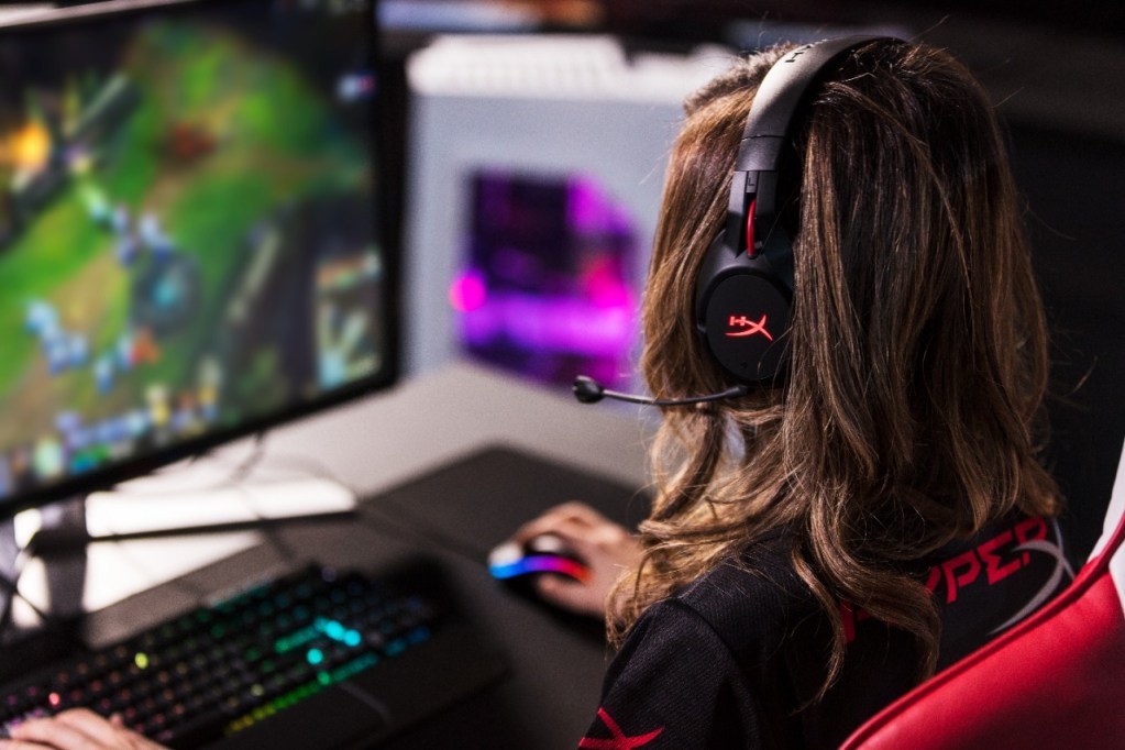 Persona con auriculares gaming utilizando una computadora para jugar, enfocada en la pantalla donde se muestra un juego en acción.