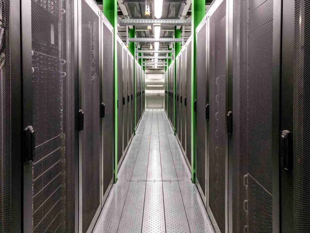 Pasillo en un centro de datos con servidores en estantes metálicos, en un ambiente industrial.