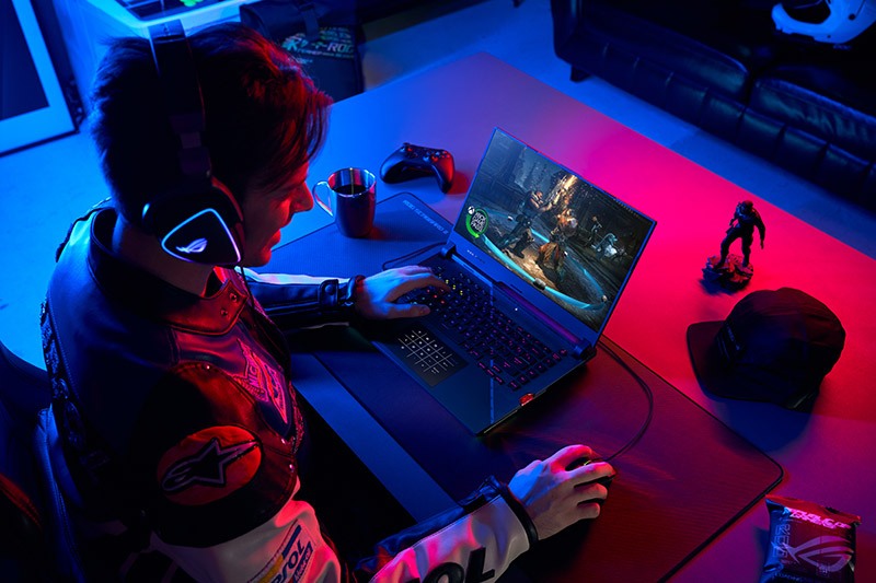 Persona jugando videojuegos en una laptop gamer en un entorno de iluminación suave y colorida, con auriculares y un control cerca.