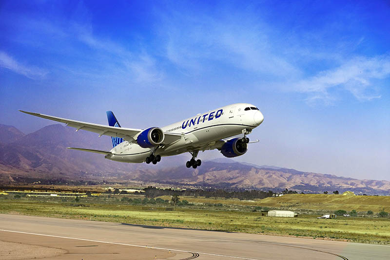 Avión Boeing 787-9 Dreamliner de United Airlines despegando frente a un paisaje montañoso y un cielo azul.