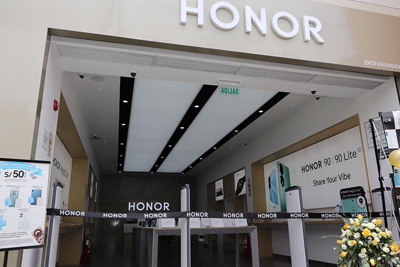 Entrada de una tienda Honor con exhibición de productos, incluyendo el modelo HONOR 90 Lite. Se observa una decoración minimalista y moderna.