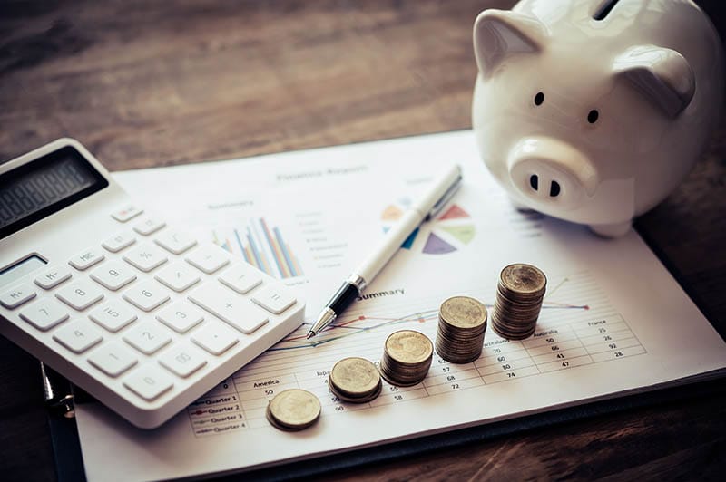 Calculadora, monedas apiladas y alcancía sobre un informe financiero.