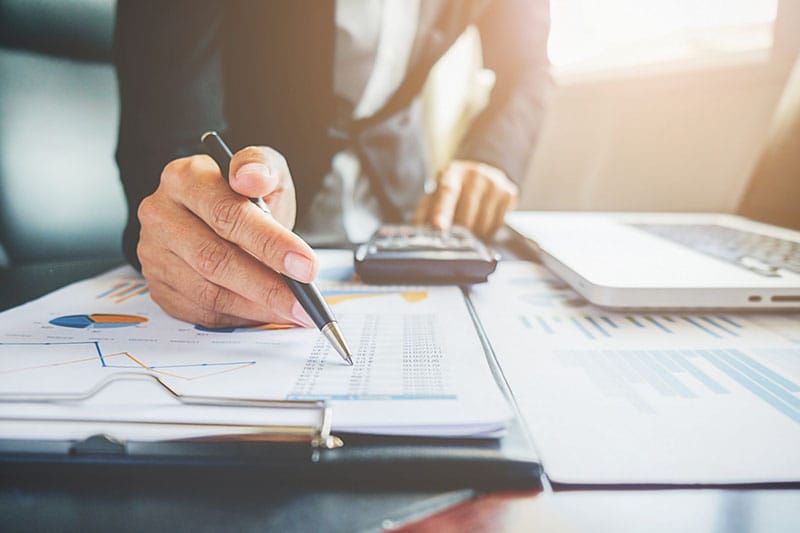 Persona revisando informes financieros y gráficos en una oficina con laptop y calculadora.