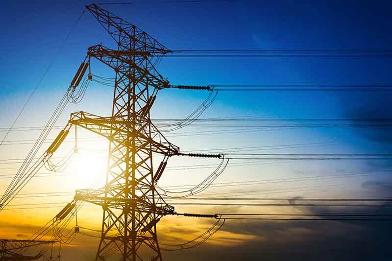 Torre de alta tensión contra un fondo de cielo al atardecer, con alambres eléctricos visibles.