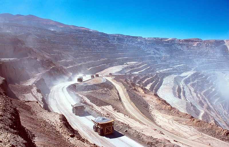 Camiones de minería en una rampa de un gran yacimiento, con capas expuestas de tierra en un paisaje desértico.