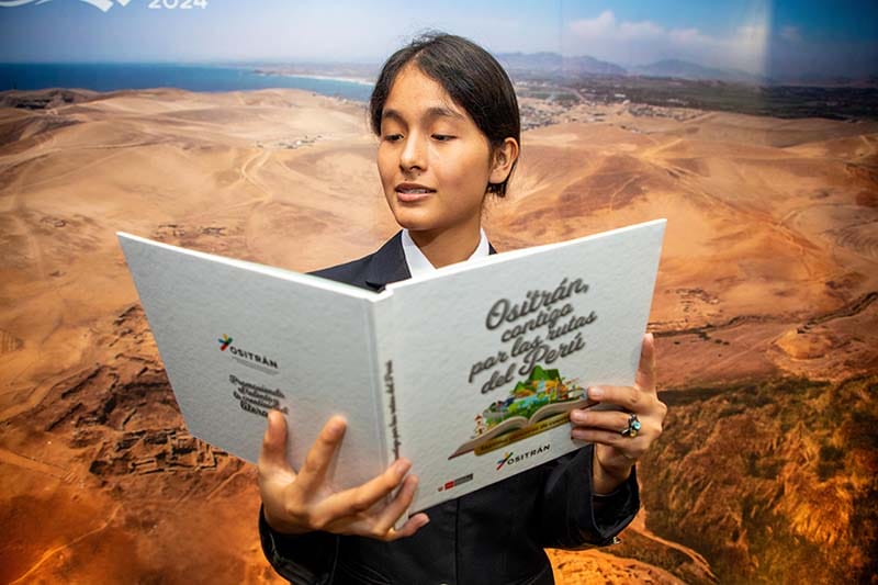 Una joven leyendo un libro titulado 'Ositrán, contigo por las rutas del Perú' con un paisaje árido y costero de fondo.