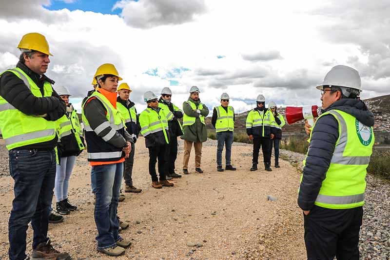 Delegación de expertos en remediación ambiental, en visita técnica en proyectos en Perú, con atuendos de seguridad y casco, mientras un orador presenta información.