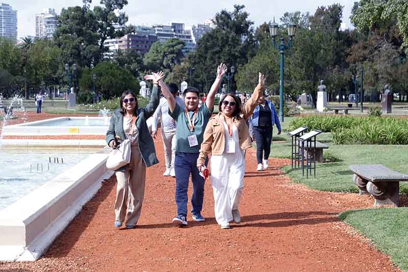 Grupo de personas sonriendo y levantando las manos en un parque, con fuentes y áreas verdes de fondo durante un evento organizado por Yanbal.