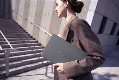 Una mujer elegante lleva una laptop en la mano mientras camina por un entorno urbano con escaleras y paredes arquitectónicas.