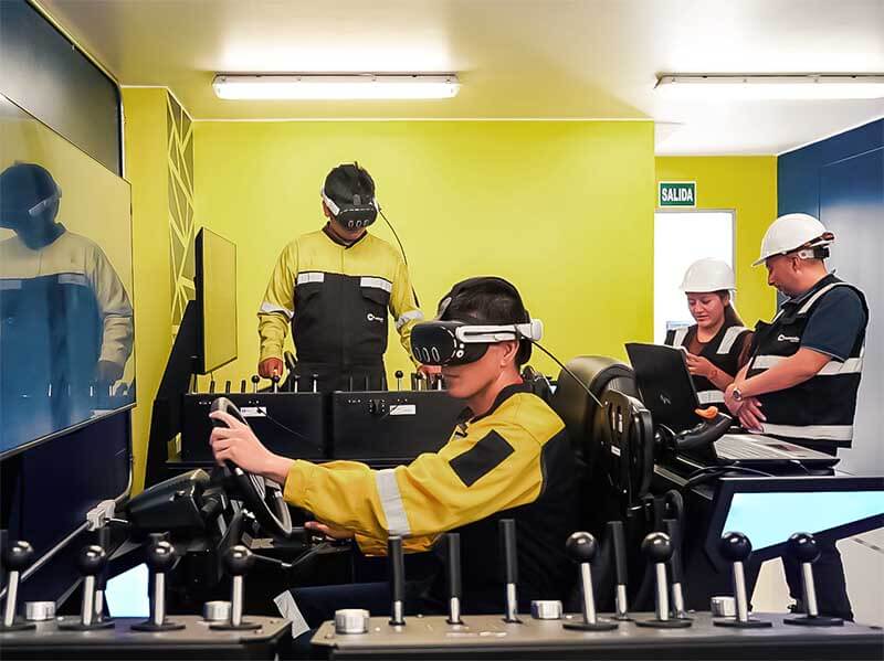 Estudiantes en sala de simuladores de realidad virtual, con diferentes equipos de minería y personal observando.