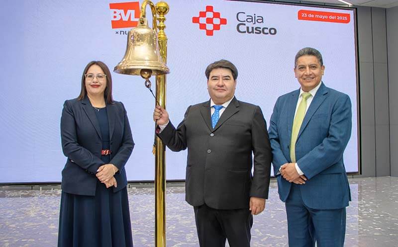 Tres representantes de Caja Cusco posan frente a una gran campana en un evento de presentación de resultados financieros, celebrando su ingreso al Mercado de Valores. Se puede ver un logo de BVL y la marca de Caja Cusco en el fondo.