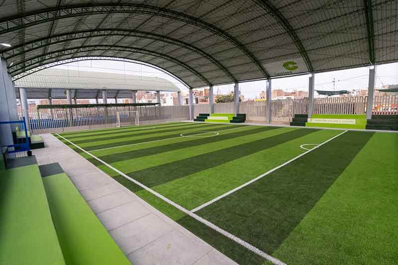 Vista interior del polideportivo remodelado en Paracas, mostrando un campo de fútbol cubierto, con césped sintético y gradas integradas, en un ambiente moderno y seguro.