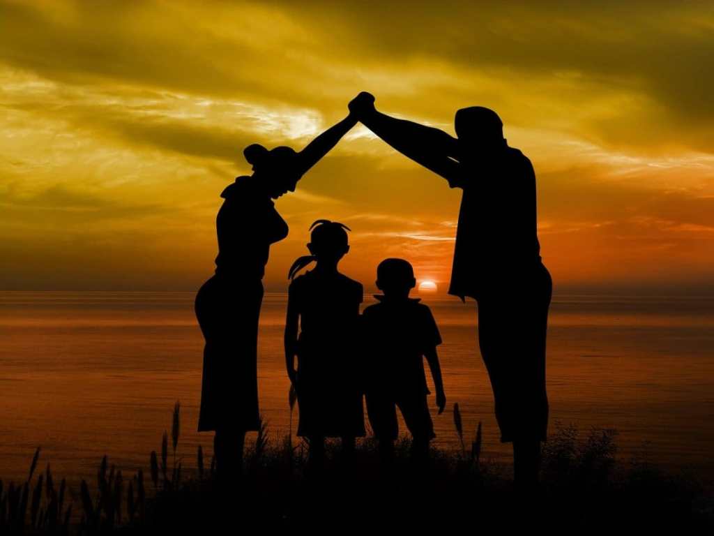 Silhouette of a family standing together against a sunset backdrop by the ocean.