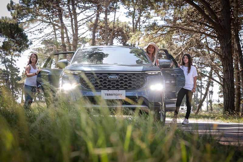 Una mujer y dos niñas están junto a un vehículo Ford Territory en un entorno natural, rodeadas de árboles y pasto.