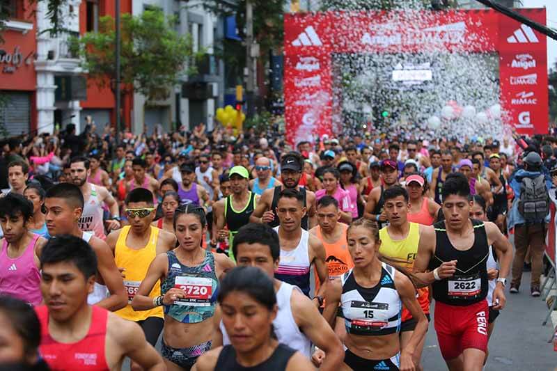 Grupo de corredores participando en una carrera, con un fondo festivo y una gran meta al fondo.