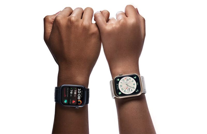 Dos manos que llevan relojes inteligentes, uno negro mostrando estadísticas de salud y otro en blanco con una esfera de reloj tradicional.