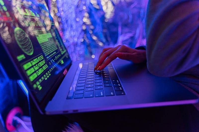 Persona utilizando una laptop en un ambiente iluminado con luces de colores, enfocándose en la pantalla que muestra gráficos y datos de seguridad cibernética.
