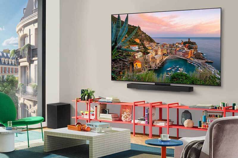 Sala de estar moderna con un televisor OLED LG montado en la pared, mostrando una imagen de un paisaje costero. Muebles de colores brillantes y decoración contemporánea.
