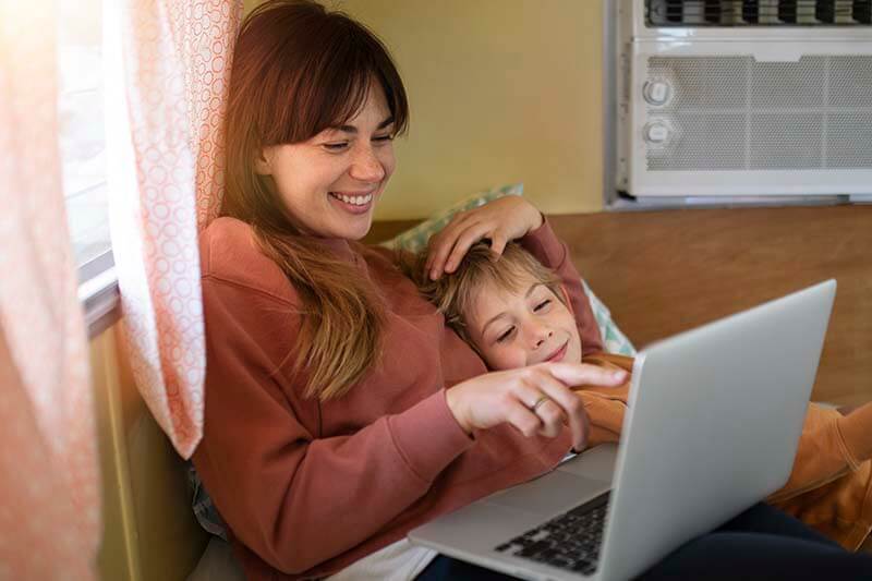 Mujer sonriente interactuando con un laptop mientras está sentada junto a un niño en un ambiente acogedor.