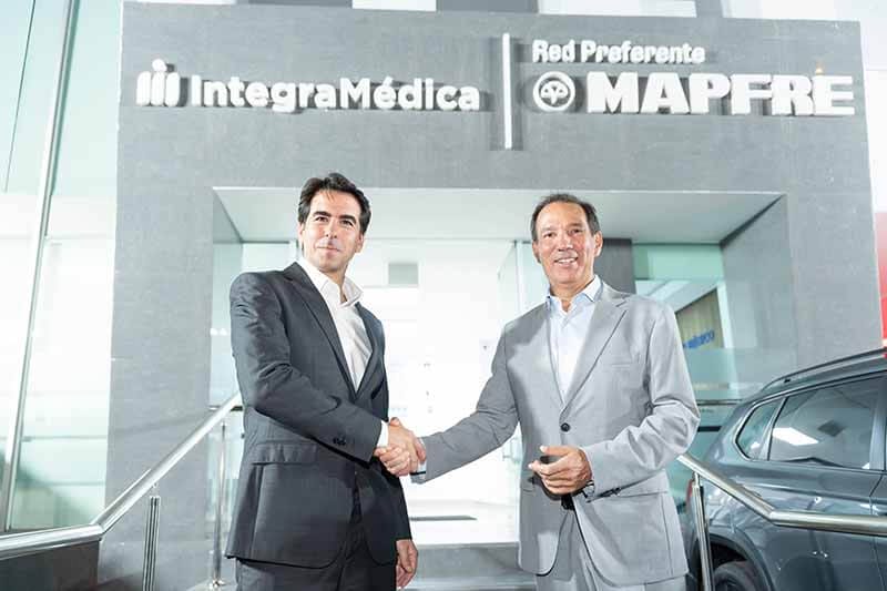 Dos hombres dando un apretón de manos frente a un edificio que muestra los logos de IntegraMédica y MAPFRE.