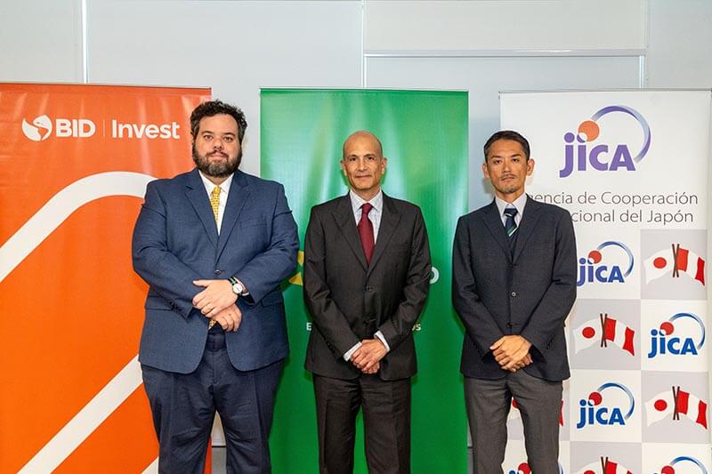 Tres representantes de instituciones financieras, con banderas de BID Invest y JICA de fondo, durante la firma de un contrato de financiamiento para Mibanco.