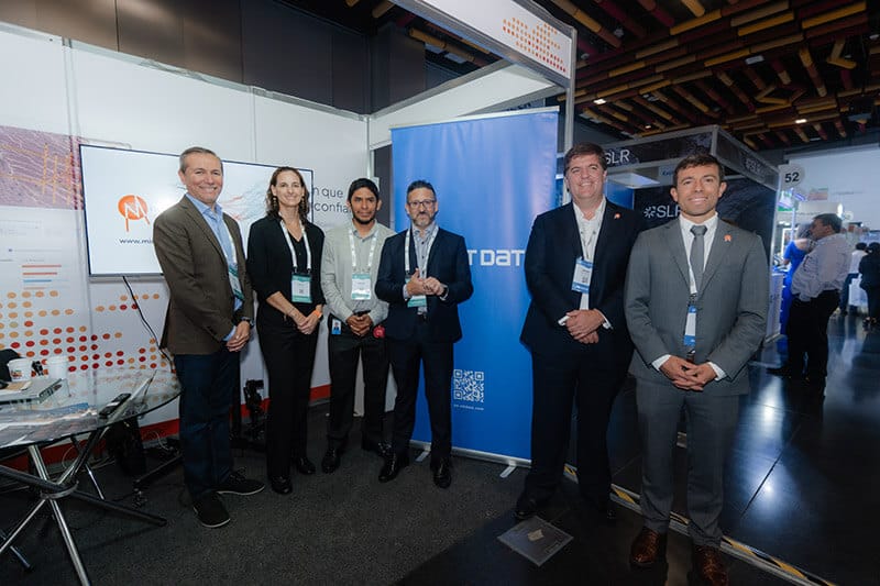 Grupo de personas de pie frente a un stand con branding de NTT DATA y Mineral Forecast, en un evento relacionado con la minería.