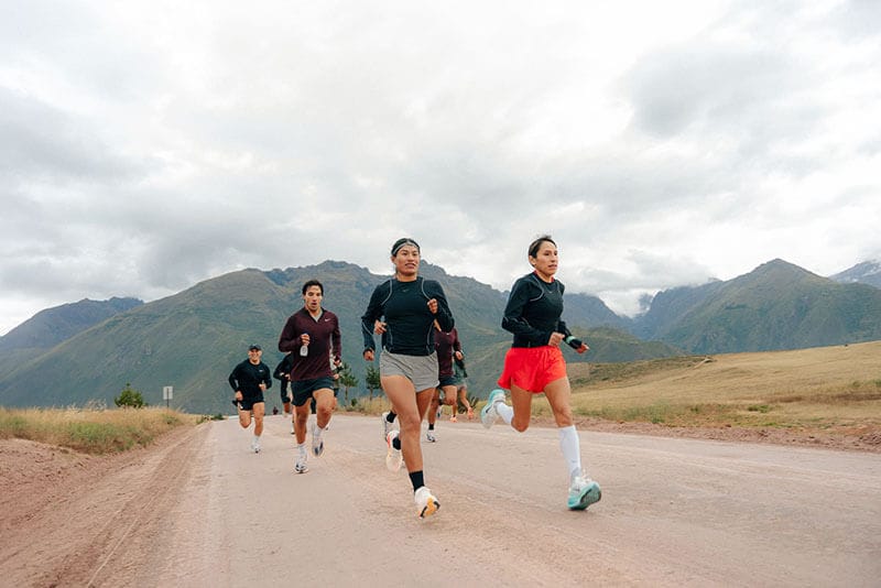 Un grupo de corredores en un camino rural del Valle Sagrado, Cusco, con montañas al fondo, mientras participan en el Nike Run Camp.