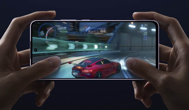Una persona sosteniendo un smartphone mientras juega un videojuego de carreras en una pantalla AMOLED.