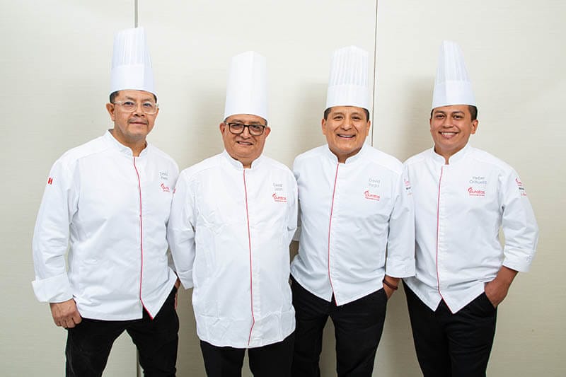 Cuatro chefs de pastelería de Puratos posando juntos, vistiendo chaquetas blancas y gorros de chef, sonriendo para la cámara en un entorno profesional.