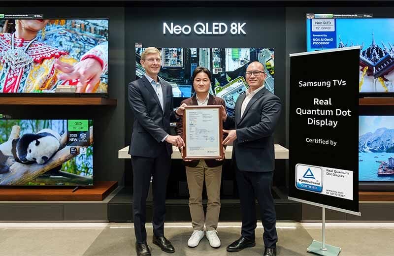 Tres personas sosteniendo un certificado de 'Real Quantum Dot Display' de TÜV Rheinland, en un showroom de televisores Samsung Neo QLED 8K.