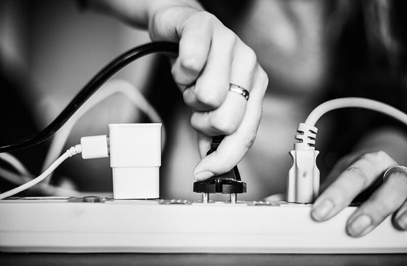 Una mano desconectando un enchufe de una regleta eléctrica, con varios cables conectados.