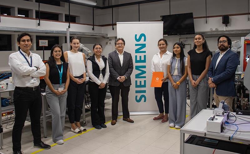 Grupo de estudiantes y profesores reunidos en un laboratorio junto a un banner de Siemens, celebrando la edición del programa Potencia tus conocimientos en Eficiencia Energética.