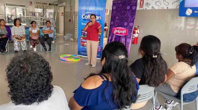 Mujeres reunidas en una charla sobre autoaceptación y sororidad, con una presentadora hablando en un ambiente de apoyo comunitario.
