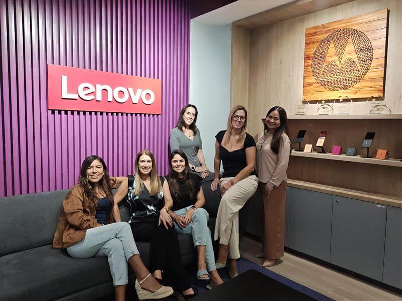 Grupo de mujeres sentadas y de pie en un ambiente de oficina de Lenovo, junto al logotipo de la compañía, promoviendo el liderazgo femenino e inclusión.