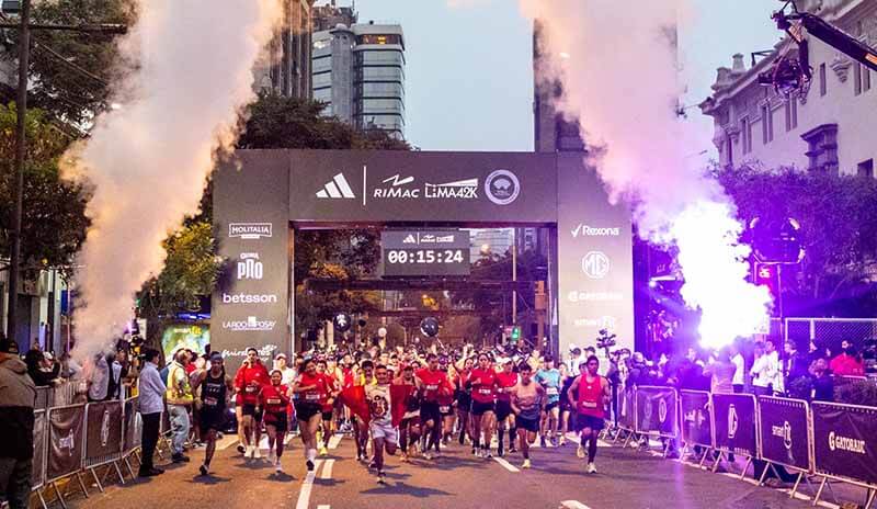 Atletas corriendo en la maratón adidas | RIMAC Lima 42K, con humo y luces en la salida de la carrera.