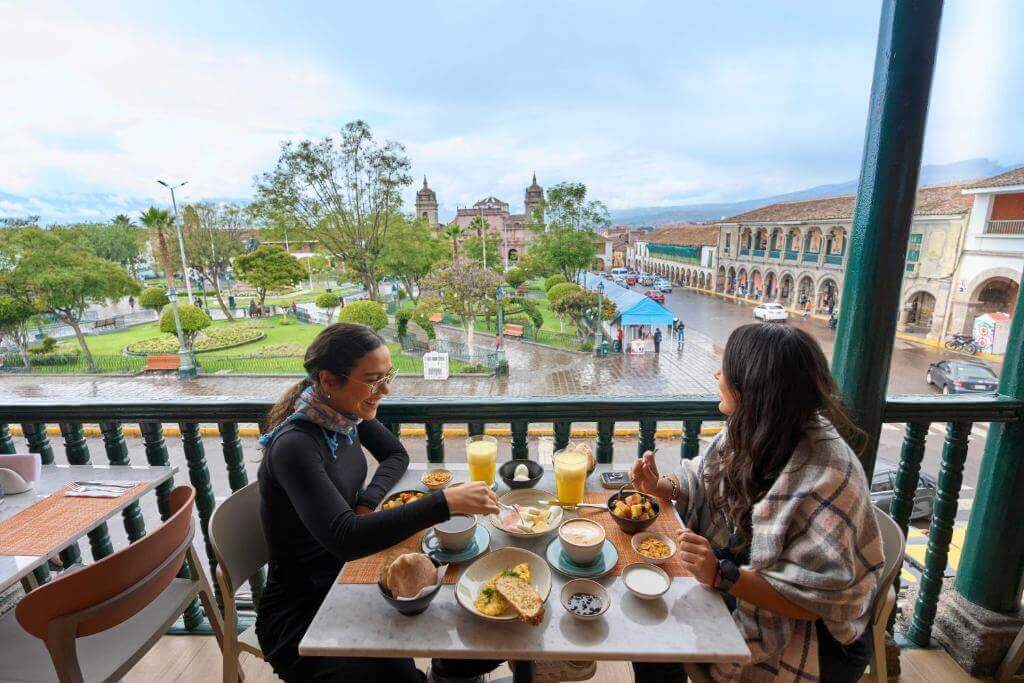 Dos personas disfrutando de un desayuno en una terraza con vista a un parque y la arquitectura local en Ayacucho, Perú.