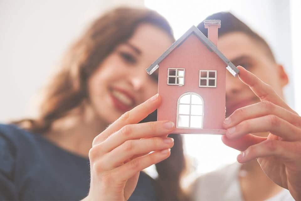Pareja sosteniendo una pequeña casa de juguete, simbolizando la búsqueda de un nuevo hogar.