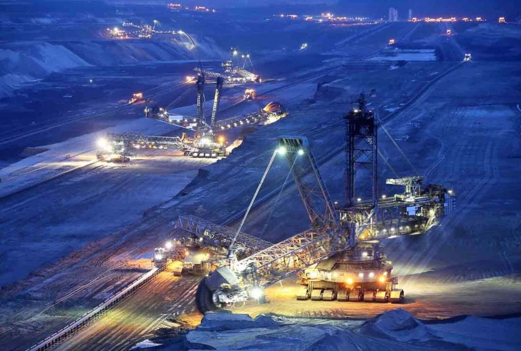Vista nocturna de una operación minera, con maquinaria pesada iluminada trabajando en la extracción de minerales en un terreno amplio.