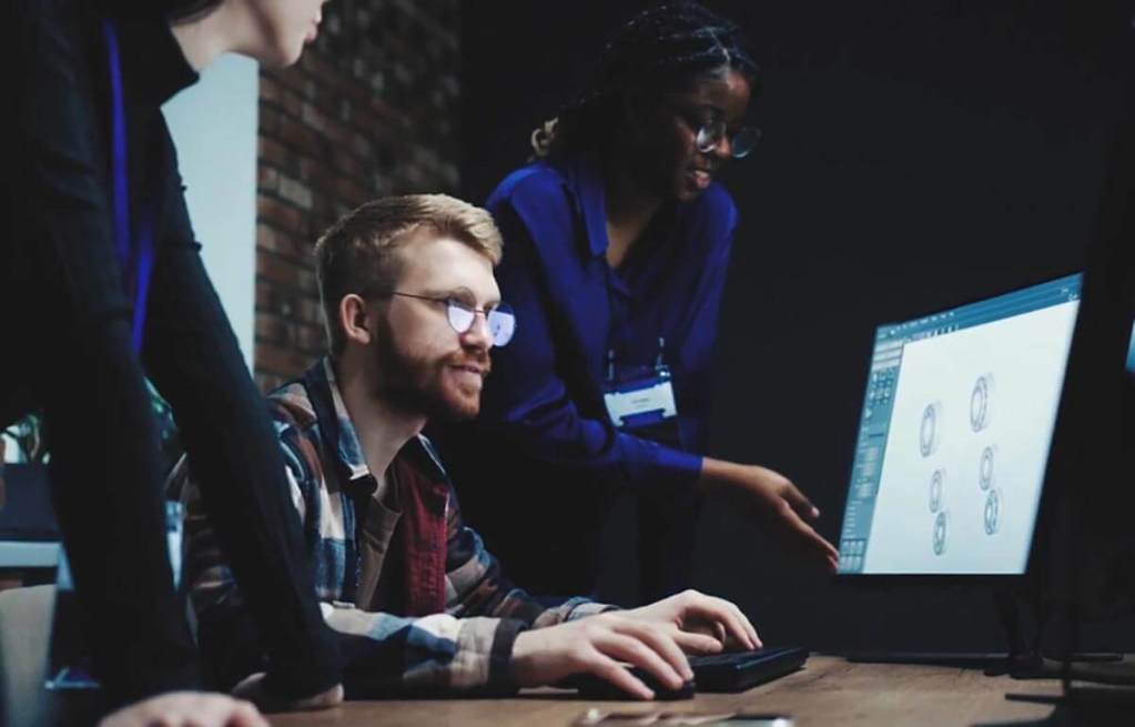 Grupo de personas colaborando frente a una computadora, trabajando en un proyecto de diseño con gráficos en pantalla.