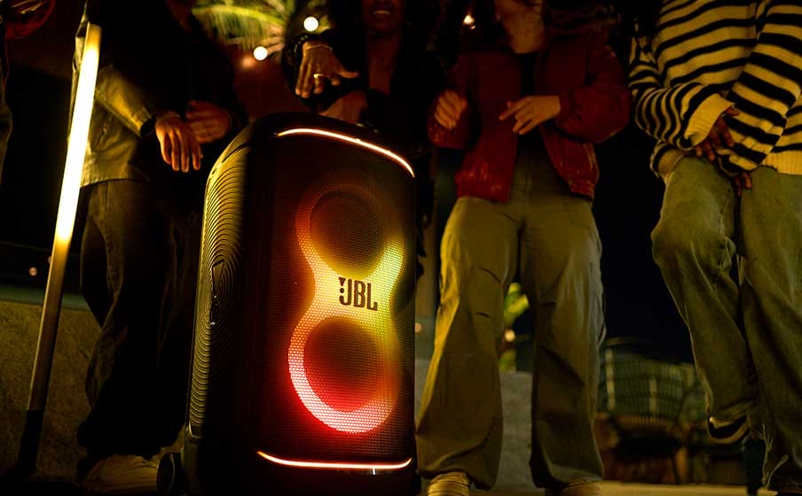 Grupo de personas disfrutando de una fiesta cerca de un altavoz JBL PartyBox 520 iluminado, con luces LED brillantes en un ambiente nocturno.
