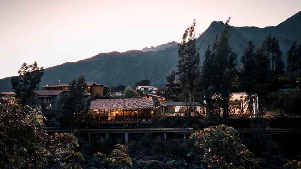 Vista del QASA Valle Sagrado en el atardecer, rodeado de montañas y naturaleza, mostrando su arquitectura rústica y acogedora.