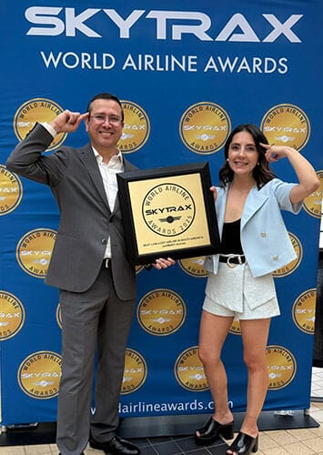 Dos personas sosteniendo un premio en un evento de los World Airline Awards, con un fondo azul que presenta el logo de Skytrax.