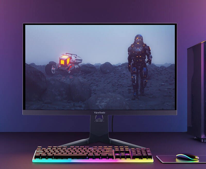Monitor gaming ViewSonic XG275D-4K de 27 pulgadas mostrando un paisaje de videojuego con un personaje y un vehículo, acompañado de un teclado y mouse RGB en un escritorio.