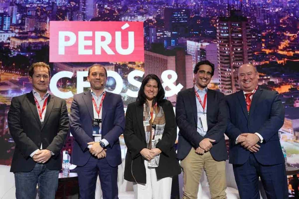 Grupo de profesionales posando en el escenario del PERU CEOs & Leaders Summit 2025, con un fondo iluminado de la ciudad.