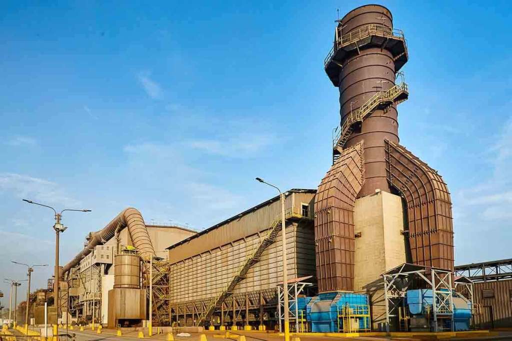 Planta industrial de Aceros Arequipa con estructuras metálicas y chimeneas bajo un cielo azul claro.