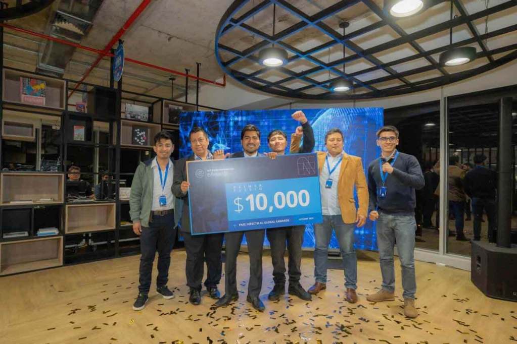 Grupo de seis personas posando con un cheque de premio de USD 10,000 en un evento de entrega de premios, rodeados de confeti en el suelo.