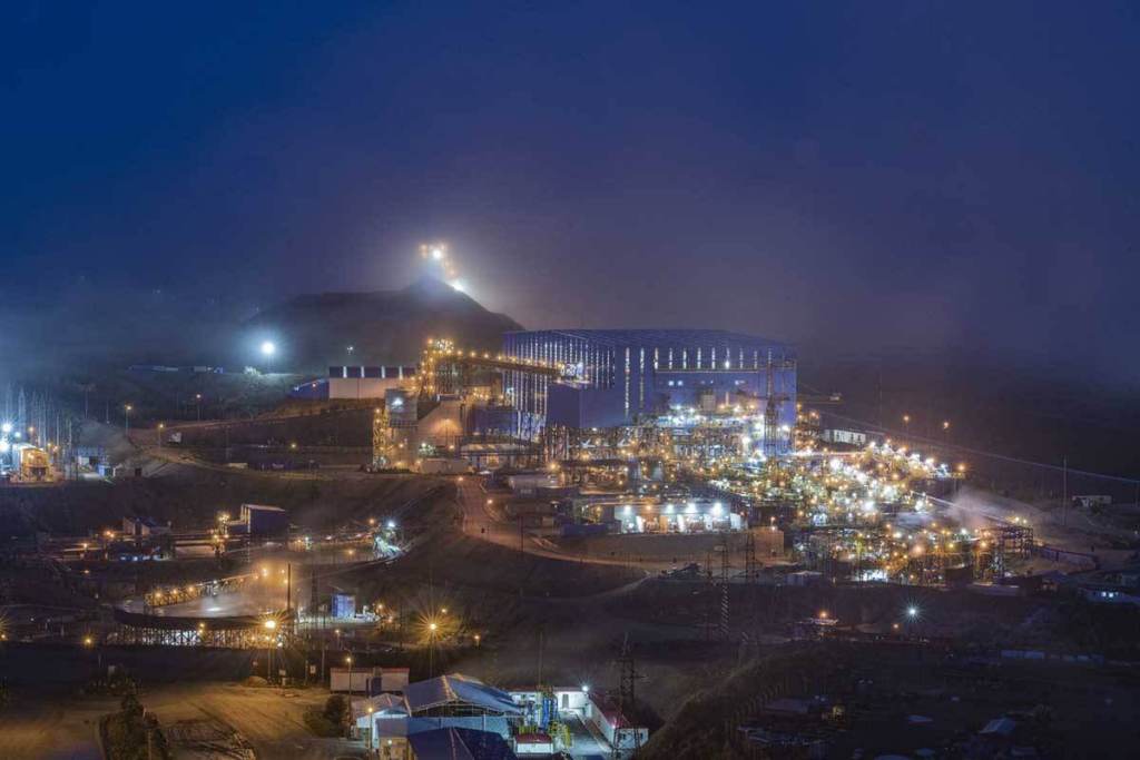 Vista nocturna de la operación minera Antapaccay, con instalaciones iluminadas y un ambiente neblinoso.
