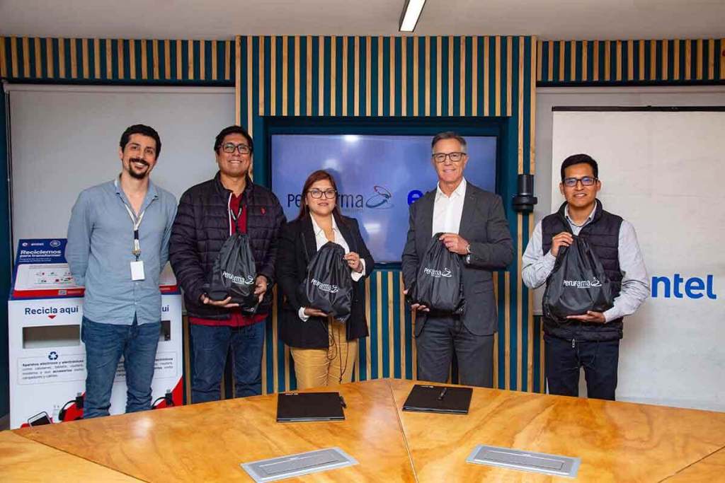Representantes de Entel y Perufarma sosteniendo bolsas en un evento de alianza estratégica sobre reciclaje de residuos electrónicos, con contenedores de reciclaje visibles en el fondo.