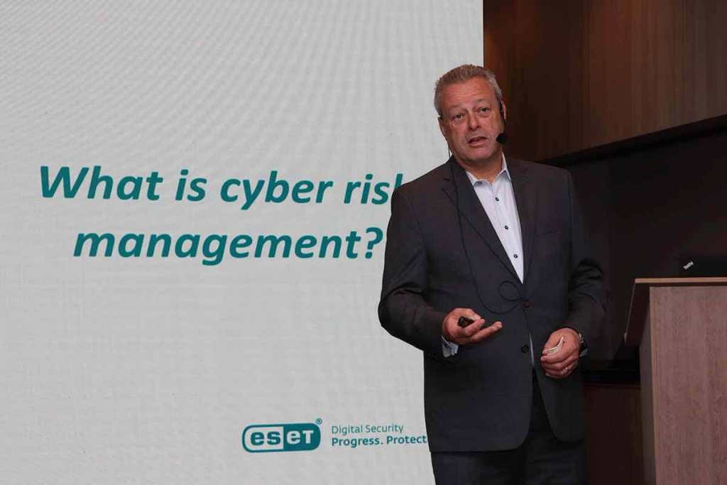 Presentador de ESET hablando sobre la gestión del riesgo cibernético en un evento de ciberseguridad, con una pantalla que muestra la frase 'What is cyber risk management?'